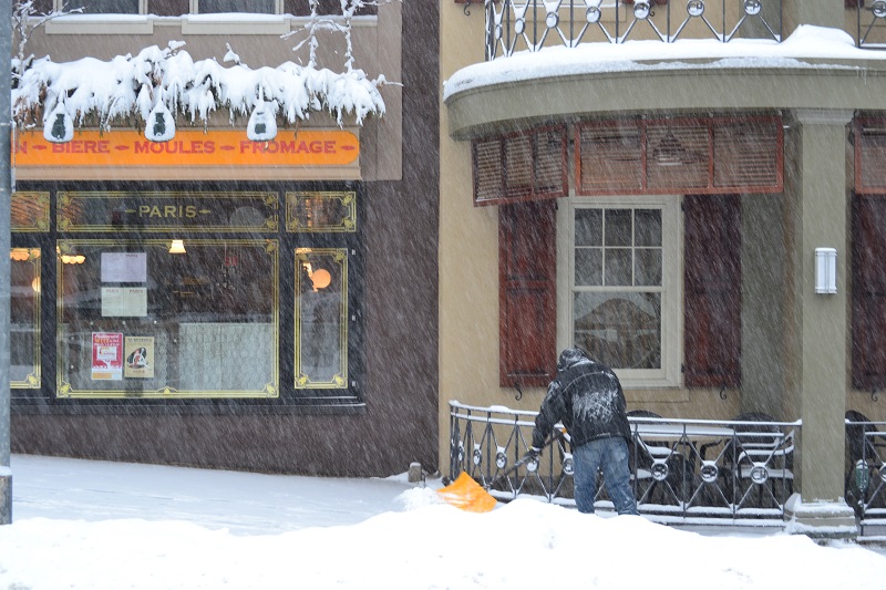 A well-bundled gentleman shovels snow from a sidewalk in front of the Chestnut Hill Hotel.